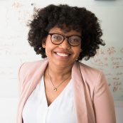 a woman with glasses smiling in front of a whiteboard.
